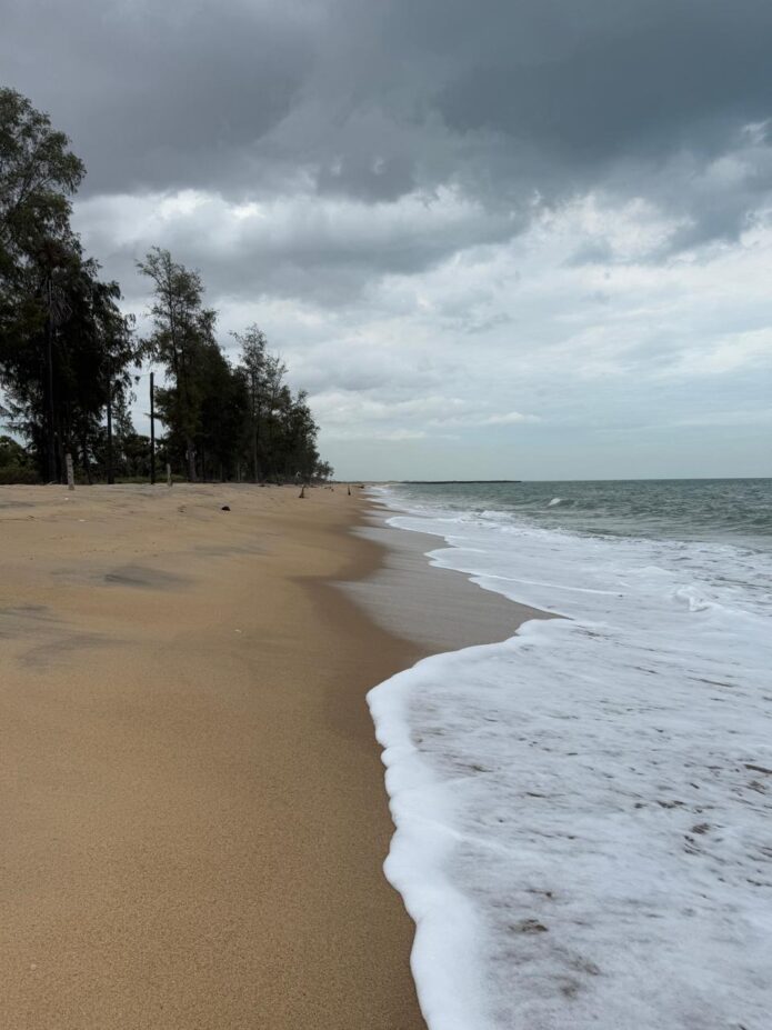 A serene Sayalkudi beach with gentle waves, empty sands, and a wide, calm sea meeting the sky.
