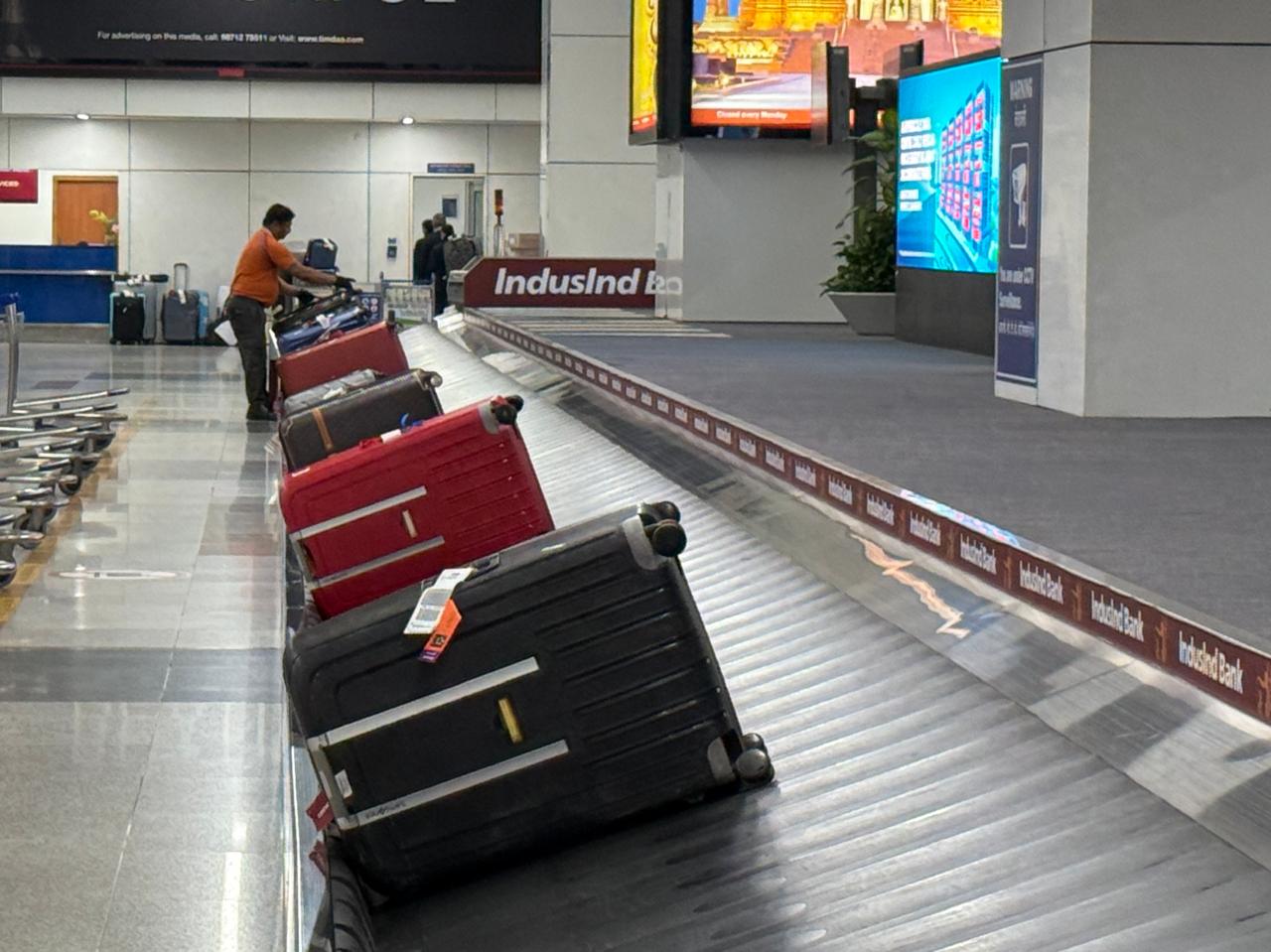 A baggage handler in an orange shirt arranges suitcases on the carousel at Delhi's Terminal 3