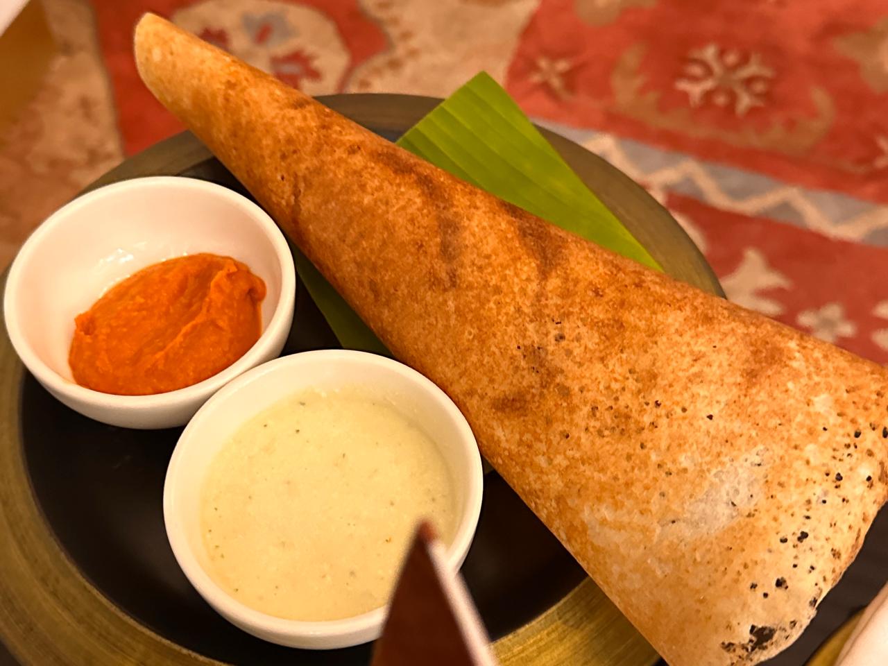 Crispy masala dosa served on a banana leaf with tomato and coconut chutney