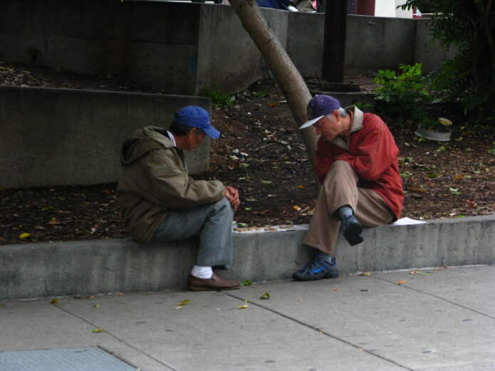 Two older men playing a board game on a kerb, choosing human friction over agreeable AI.