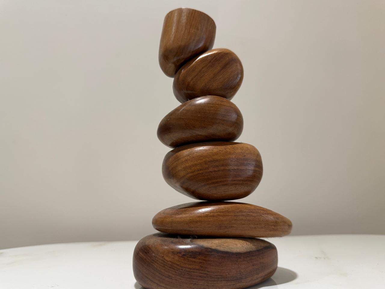 Six smooth polished walnut stones stacked into a balanced cairn on a pale marble surface.