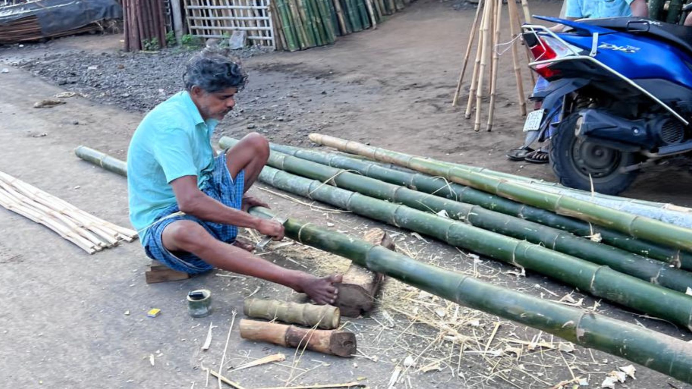A craftsman splitting bamboo by hand on a roadside in Tamil Nadu, outside a bamboo yard
